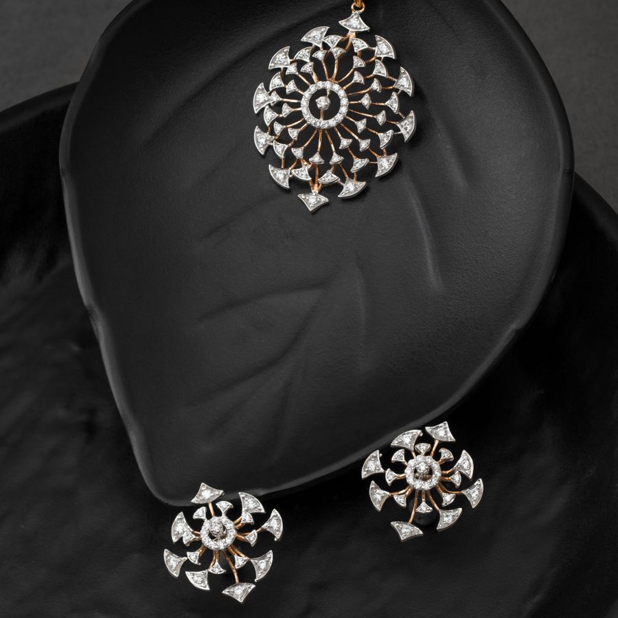 Gold and diamond pendant and earrings set on a dark leaf-shaped surface